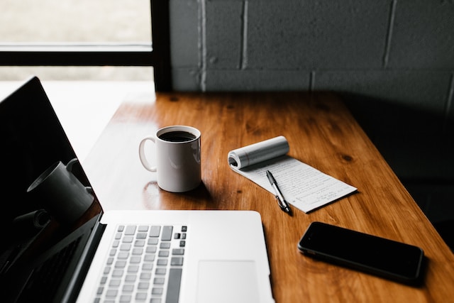 Laptop, coffee mug and notebook on top of wooden table